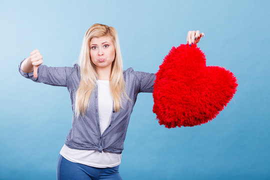 Woman holding red heart showing thumb down