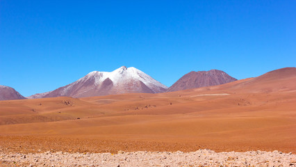 Fototapeta na wymiar Natural beauty of unspoiled desert landscape. Colorful landscape of rocks, sandy valleys, and volcanic mountains with snow peaks in Atacama Desert, Chile.