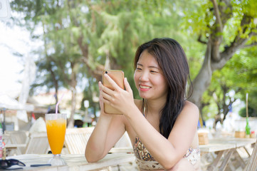 beautiful Asian Chinese woman using internet social media on mobile phone sitting at beach restaurant resort enjoying summer holidays