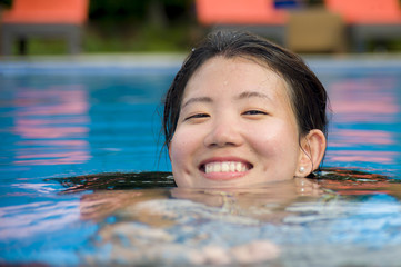 happy and pretty Chinese Asian woman enjoying cheerful and relaxed having fun smiling at swimming pool of resort hotel in Summer holiday