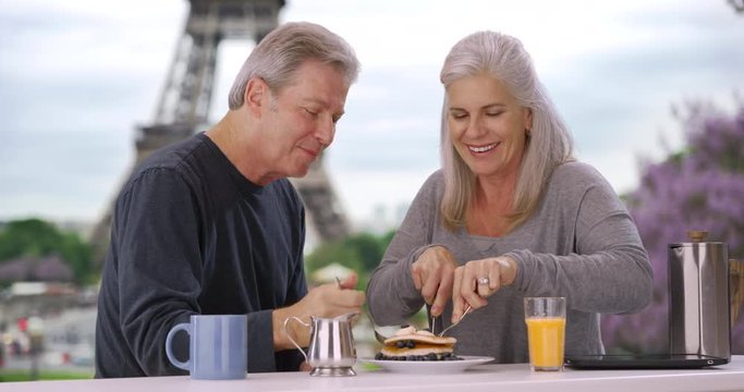 Older white male and female near Eiffel Tower eat delicious breakfast pastry