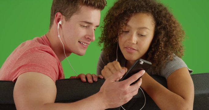 Lovely young couple listening to music on mobile device on green screen. On green screen to be keyed or composited. 