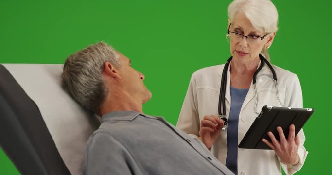 Senior woman doctor talking with elderly man patient in the office on green screen. On green screen to be keyed or composited. 