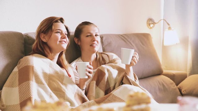 
Girlfriends are watching TV and drfinking tea at home.
