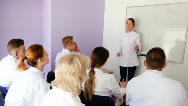 Male medical student answering near whiteboard in front of teacher and group of students in auditorium