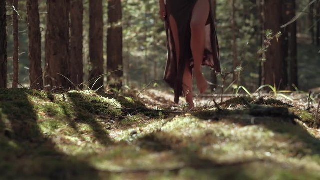 A young girl's bare feet go on a forest of soft moss, long dress, the slender legs of the models walking on camera