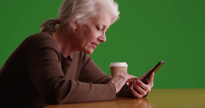 Cheerful senior woman holding credit card using mobile device to make payment online on greenscreen. Mature woman using cellphone for easy online purchase on green screen to be keyed or composited. 