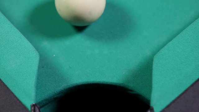 Close up of a billiard ball number 8 with black color falling into the billiard table hole