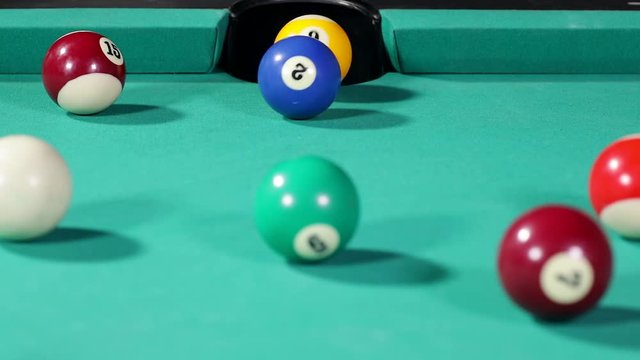 Close up of a yellow billiard ball get into the hole after hitted by the blue and white ball on the table