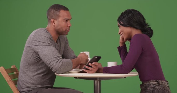 African American couple drinking coffee and browsing internet on smartphones on date on green screen. On green screen to be keyed or composited. 