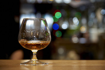 A glass of cognac on a dark background with a bright bokeh