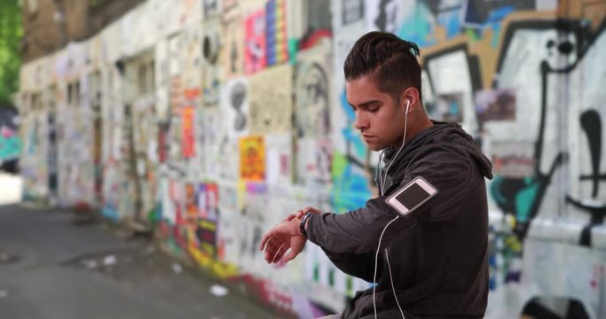 Hispanic male jogger checking fitness tracker in alley with cool graffiti