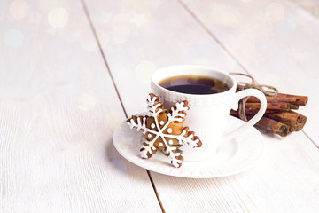 Cup of coffee with gingerbread snowflake and cinnamon sticks on white wooden table.