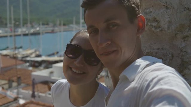 Young beautiful couple - man and woman smiling and doing selfie on the background of beautiful view of the sea and boats during holiday