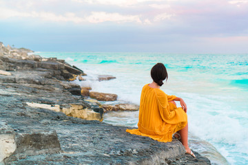 Young beautiful woman in dress on the beach with amazing view on the sea and sky