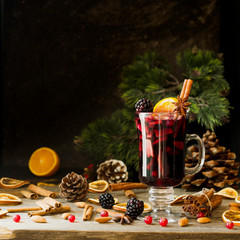 glass of hot mulled wine for the new year with ingredients for cooking, nuts and Christmas decorations