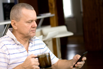 Old man using smartphone and having herbal tea at home, looking serious