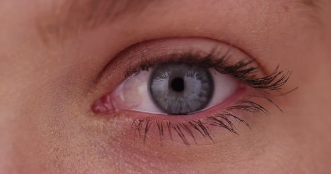Extreme close up of young Caucasian woman's blue eye, front view blinking and looking at camera on green screen. On green screen to be keyed or composited. 