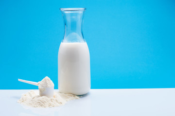 Bottle of fresh milk with powdered milk and spoon for baby on white table,blue background.
