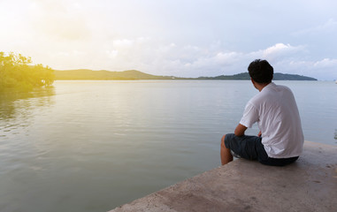 Fototapeta na wymiar Lonely asian man sitting alone on a pier on sea in phuket thailand.
