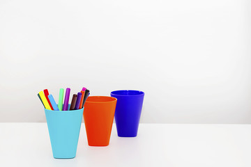 Multicolored plastic glasses with colorful pencils on a light background