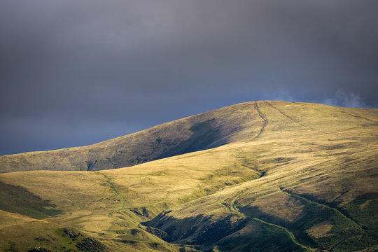 Golden light shining on hill near Sedbergh with dark clouds in background