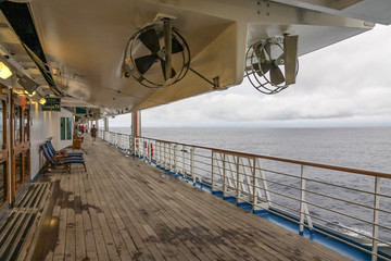 Teak lined Promenade Deck of modern cruise ship on a grey stormy day.