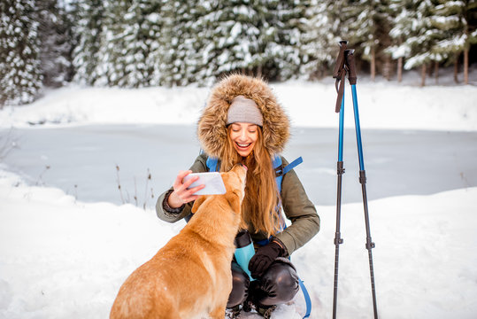 Woman having a break during the winter hiking making selfie with her dog at the snowy mountains near the lake and forest