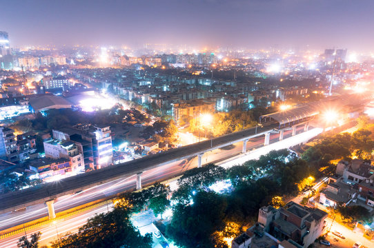 Aerial View Of The Cityscape Of Noida Gurgoan Delhi At Night  With The Elevated Metro Track And Metro Station Visible. The City Residences And Offices Are Also Clearly Visible