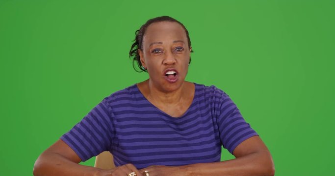 A casually dressed black businesswoman happily talks to the camera on green screen. On green screen to be keyed or composited. 