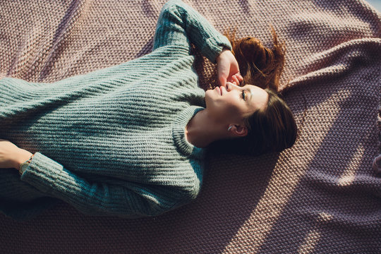 Beautiful sexy tan brunette woman posing in bedroom, wearing cozy grey sweater and knitted socks. Rest, sleeping, comfort concept. Close up of young woman lying in bed at home. Scandinavian home.