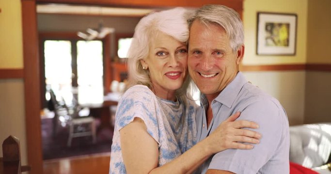 Smiling elderly couple sitting at home looking at camera