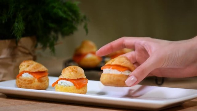 Female hands put profiteroles with salmon in a white plate