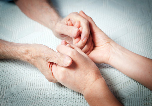 Old and young holding hands on light background, closeup. Care is at home of elderly