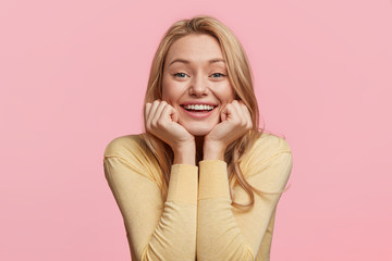 Portrait of glad smiling female model leans at hands, has broad smile, happy to recieve compliments...