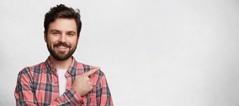 Horizontal portrait of cheerful attractive bearded male advertizes something, stands against white background with copy space for your promotional text. People, emotions, advertisment concept