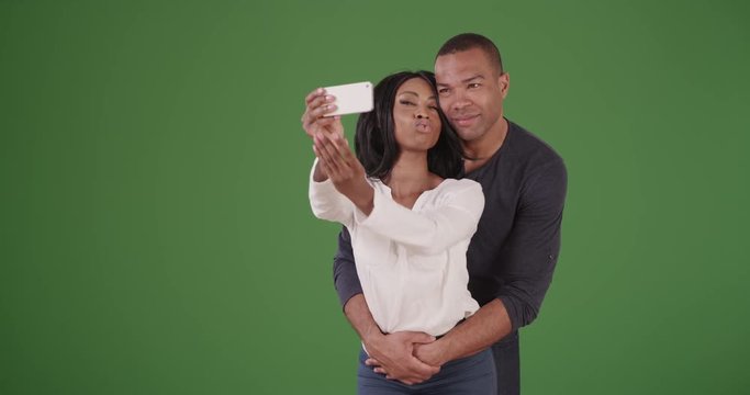 A young african American couple pose for cute selfies and kiss on green screen. On green screen to be keyed or composited. 