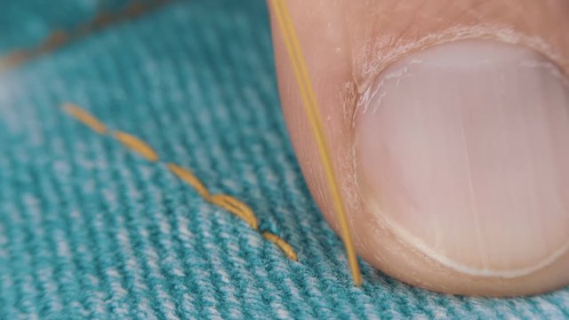 Sewing needle with a yellow thread makes a line on the jean. Macro. Closeup. Shallow depth of field
