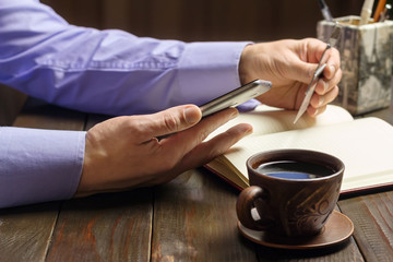 Fototapeta na wymiar Home office workplace, male hands hold a smartphone and credit card, opened notepad, cup of black coffee on dark wood working table, business, finance concept