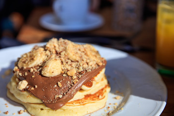 Pancakes with chocolate sauce on a white plate. Closeup view and blurred cafe background.