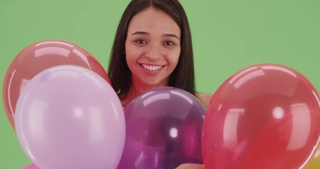 Hispanic girl playing with many multicolored balloons on green screen. On green screen to be keyed or composited.  - Powered by Adobe