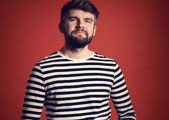 Bearded smiling emotional man in casual striped t-shirt on dark red background. Closeup portrait