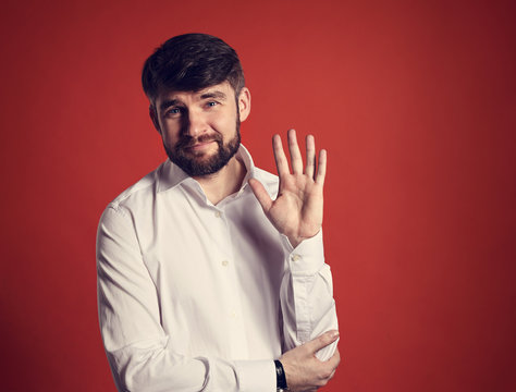Happy smiling bearded businessman waving the hand and saying hello in fashion white style shirt on dark red background. Closeup toned portrait