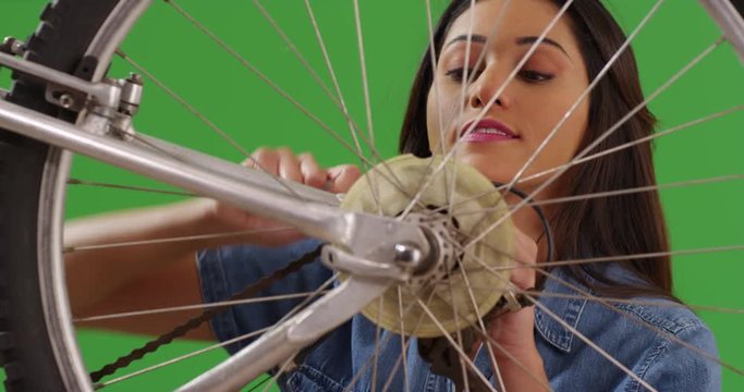 Hispanic girl fixing her bike with a socket wrench on green screen. On green screen to be keyed or composited. 