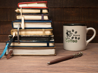 A stack of notebooks and a cup of coffee on a wooden table