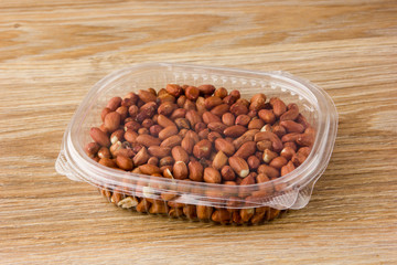 Peanuts in plastic packaging. Fresh peanuts without shell in a plastic container on a wooden table.
