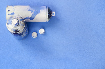 Some used blue aerosol spray cans and nozzles with paint drips lies on a blanket of soft and furry...