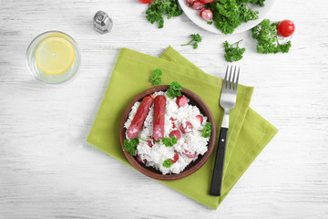 Wooden plate with rice and sausage on light background