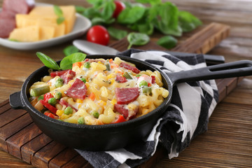 Pasta with sausage and vegetables in frying pan on wooden board