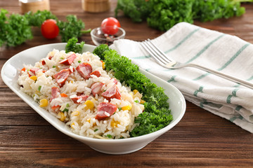 Rice with sausage and vegetables in ceramic bowl on wooden background